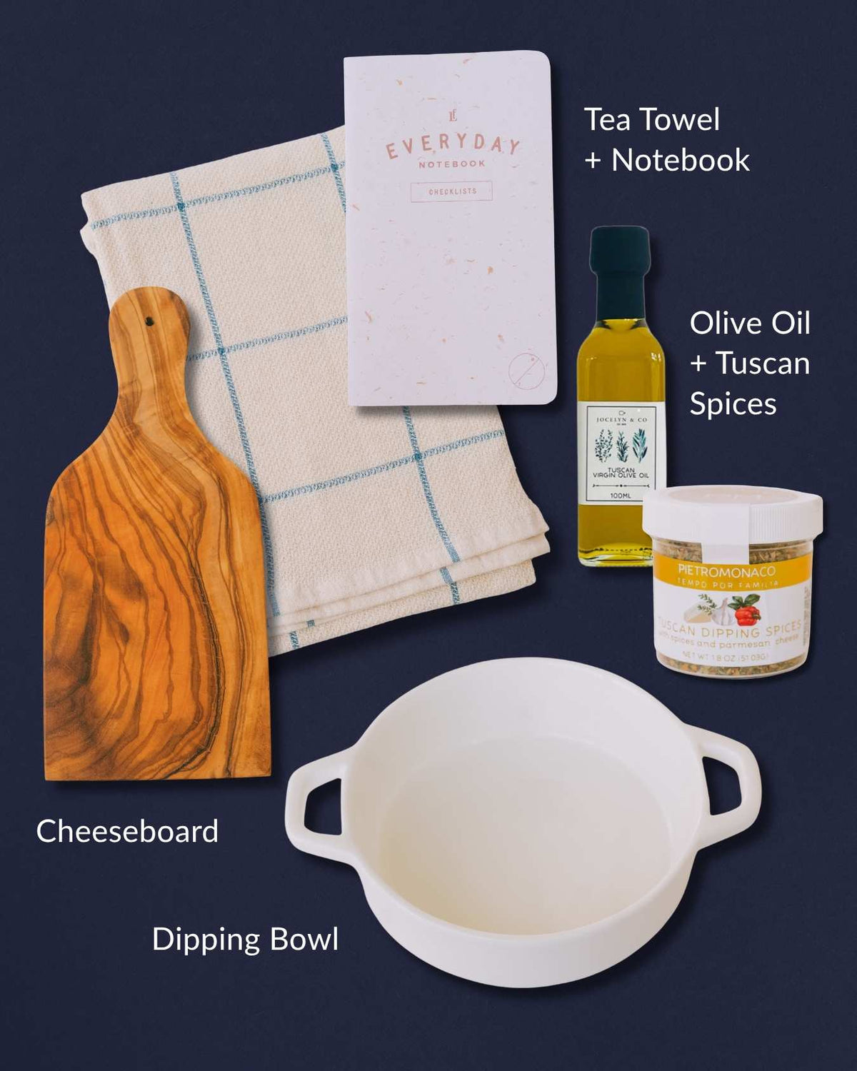 Kitchen gift set with an olive wood cheeseboard, white dipping bowl, blue-checkered towel, olive oil, spices, and a notebook.