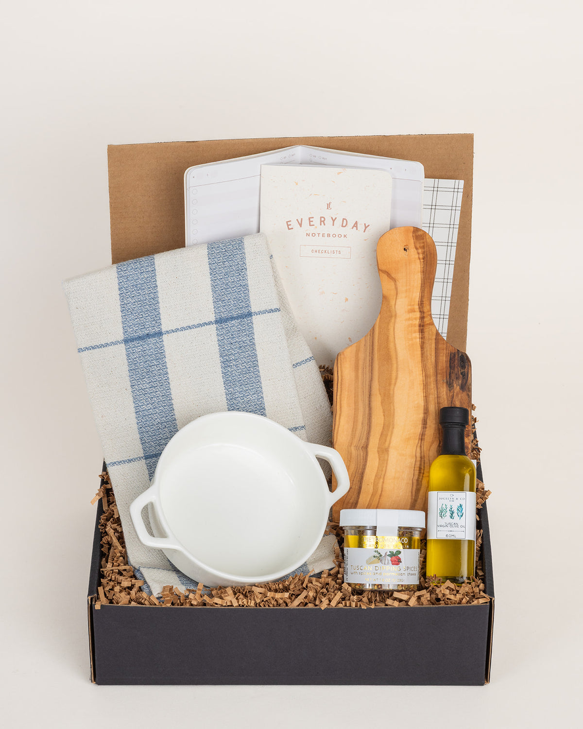 Kitchen gift set with blue plaid towel, white bowl, olive wood board, Tuscan olive oil, dipping spices, and notebook.