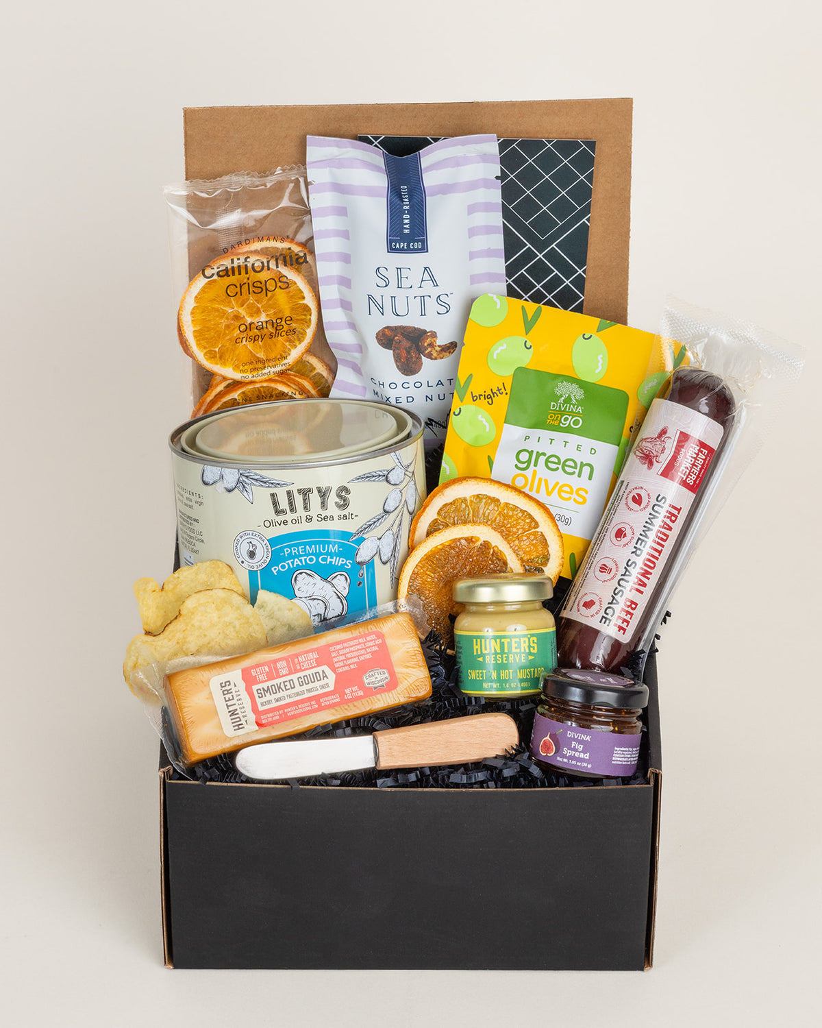 Charcuterie gift box with summer sausage, smoked gouda, potato chips, olives, fig spread, mustard, nuts, and a spreading knife.