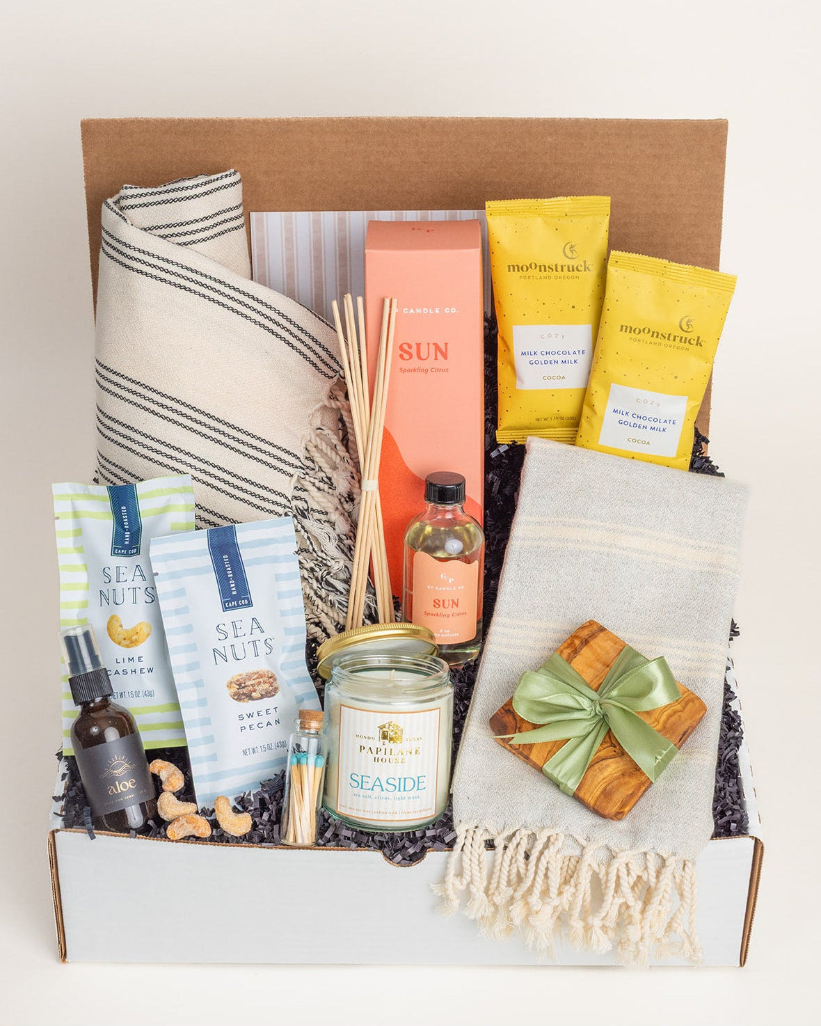 Coastal gift box with Turkish towels, olive wood coasters, Sun reed diffuser, candle, snacks, and aloe spray in a white box.