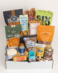 Deluxe Foodie gift box filled with assorted gourmet snacks, beef jerky, pretzels, caramel sauce, and savory treats in a white box.