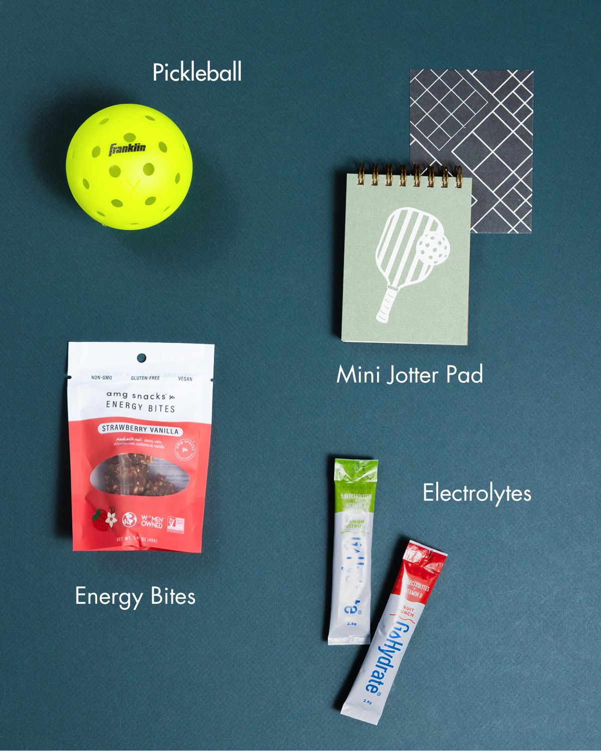 Pickleball gift set featuring a yellow ball, mini jotter pad, strawberry energy bites, and electrolyte drink sticks.