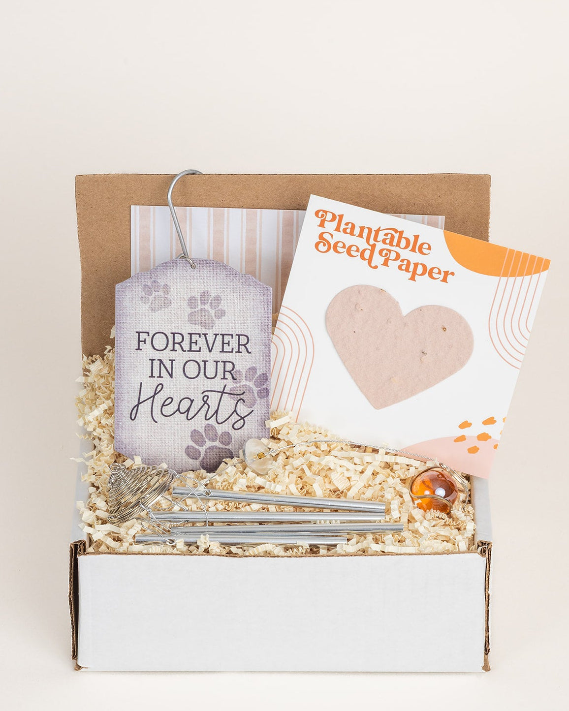 Pet memorial gift box with Forever in Our Hearts wind chimes and a heart-shaped plantable seed paper card in straw filler.