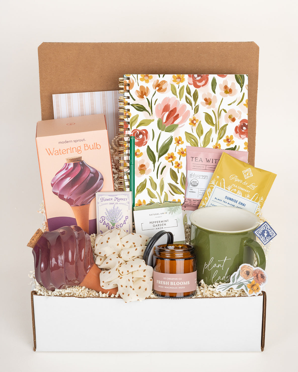 Gardener gift box featuring a floral notebook, ceramic watering bulb, plant lady mug, peppermint soap, candle, and tea packets.