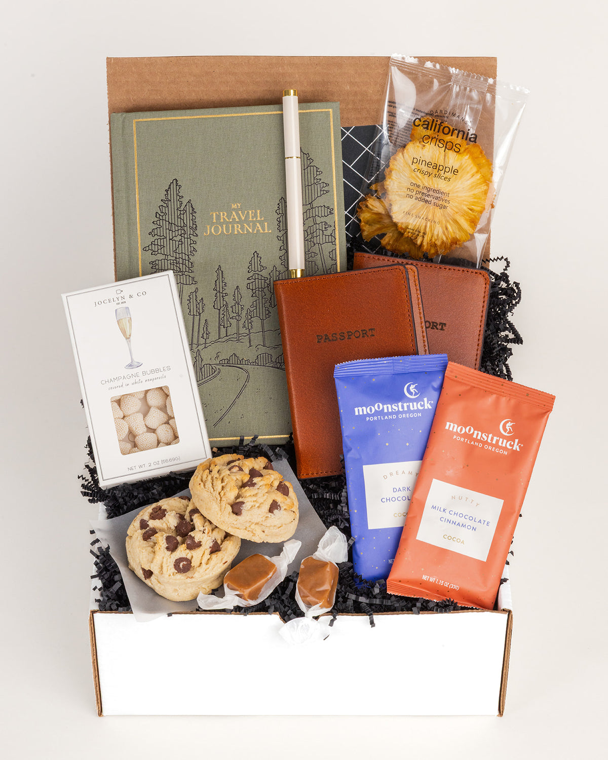Gift box for couples featuring a green travel journal, two leather passport covers, gourmet cookies, chocolates, and snacks.