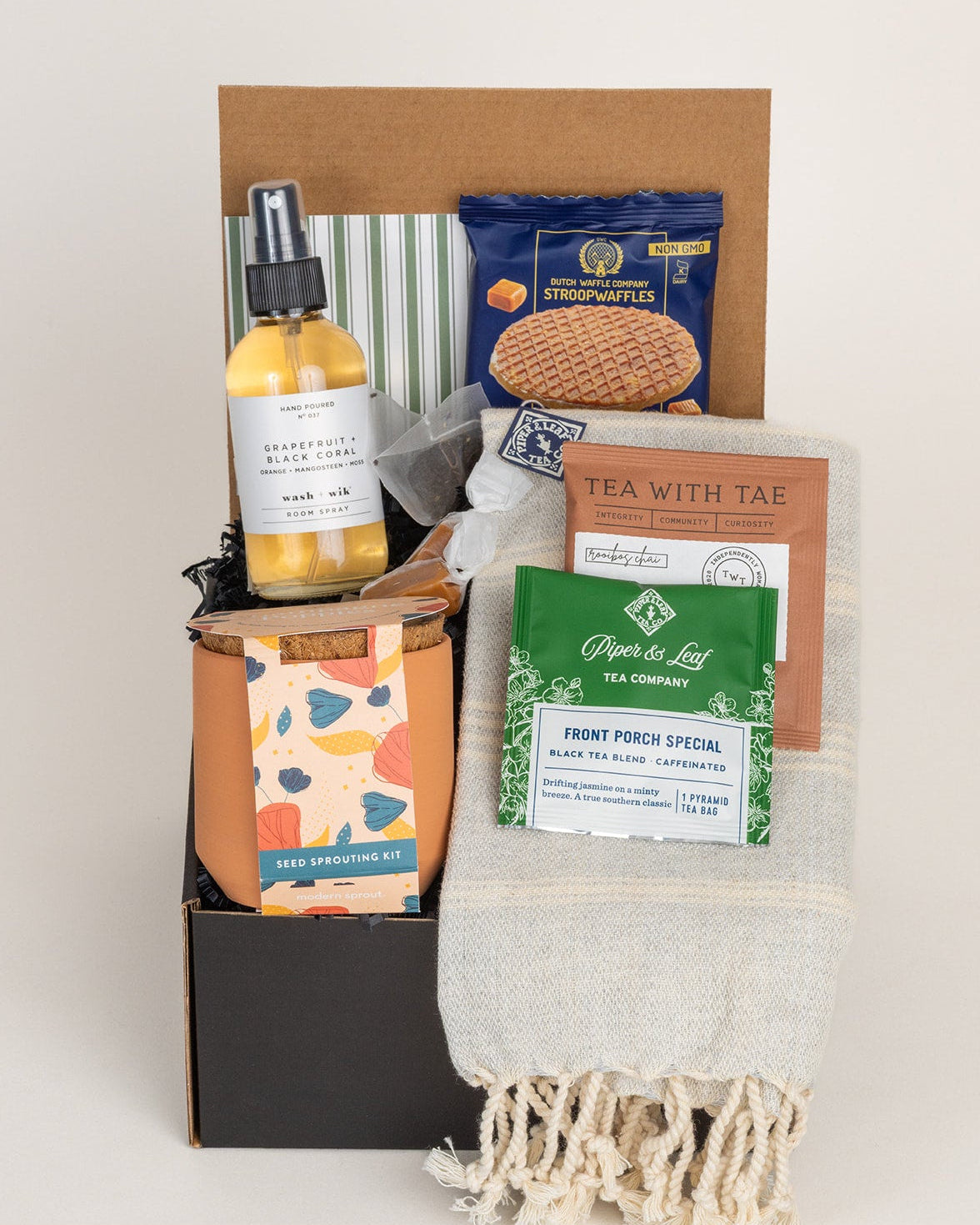 Gift box containing a terracotta seed kit, room spray, stroopwafel, two tea packets, and a fringed Turkish hand towel.