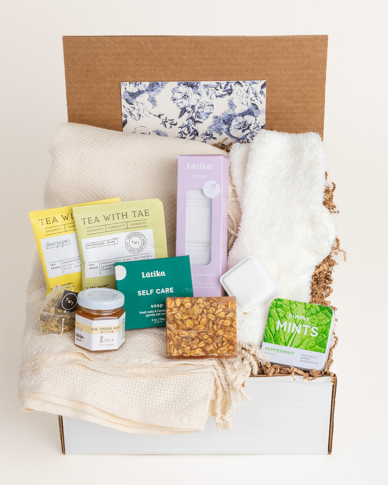 Get Well care package featuring a cream throw blanket, fuzzy socks, tea, honey, oatmeal soap, shower steamers, and mints.