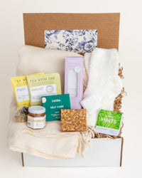 Get Well care package featuring a cream throw blanket, fuzzy socks, tea, honey, oatmeal soap, shower steamers, and mints.