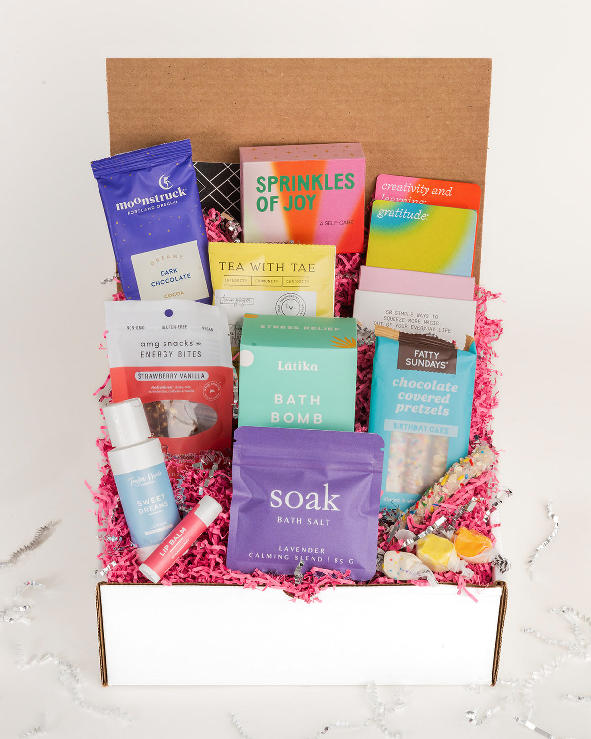 Happy Box gift set filled with colorful self-care items, snacks, bath products, and tea nestled in bright pink crinkle paper.