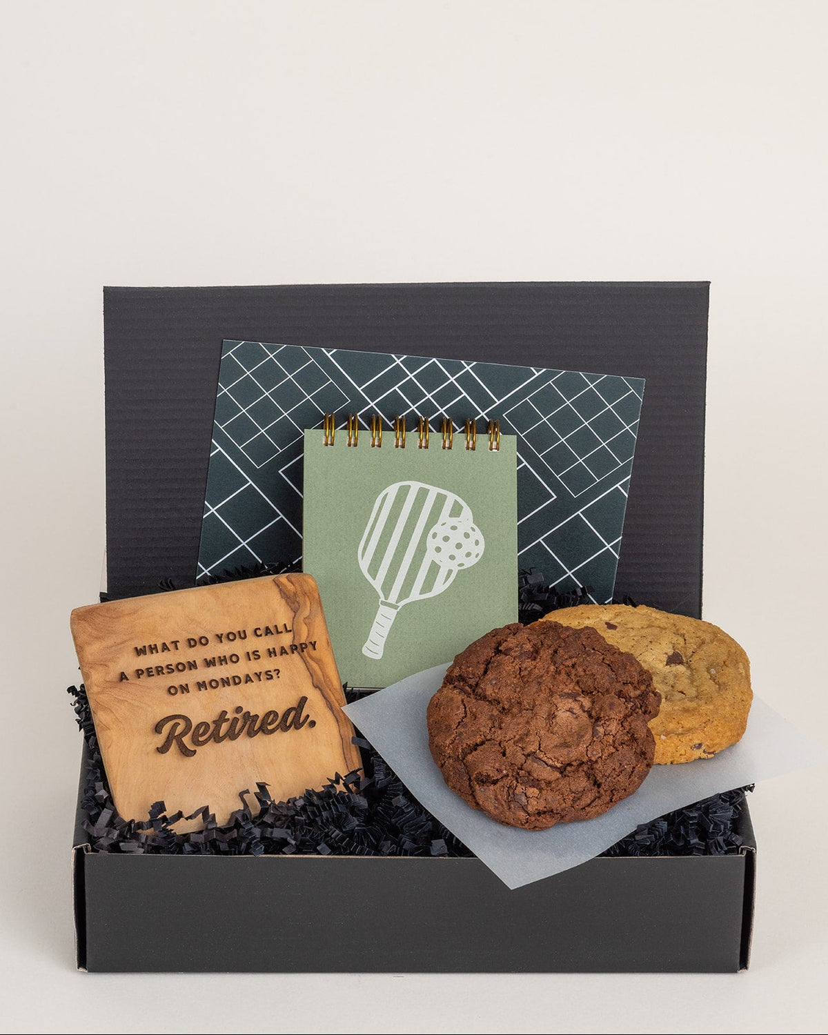 Happy Retirement gift box with an olive wood coaster, two cookies, and a pickleball-themed mini jotter pad.