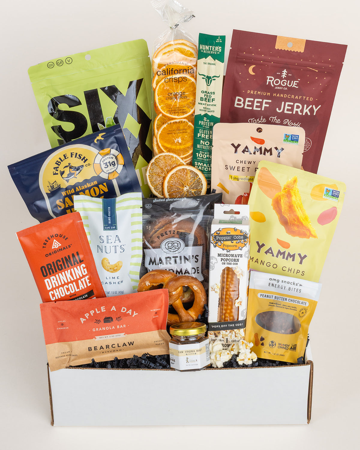 Curated gift box filled with assorted healthy snacks, including jerky, dried fruit, nuts, and popcorn in a white cardboard box.