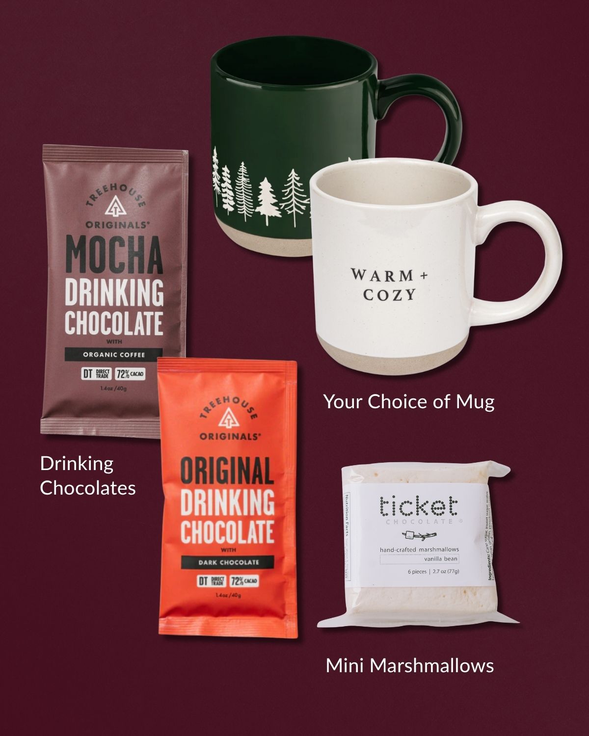 Stoneware mugs in forest green and cream with drinking chocolate packets and a bag of vanilla bean marshmallows.