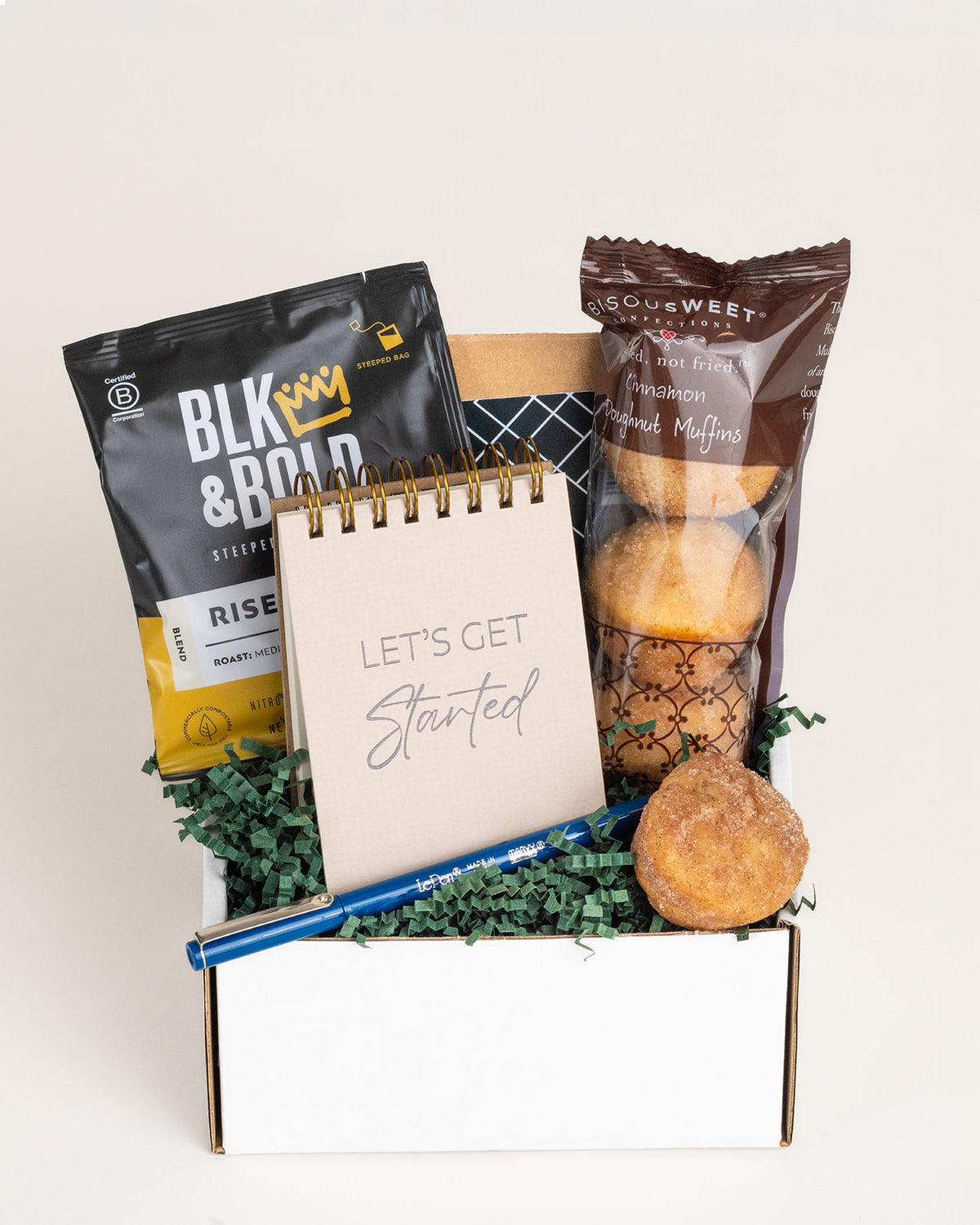 Gift box with Blk & Bold coffee, cinnamon doughnut muffins, a Let’s Get Started notepad, and a blue pen on green paper filler.