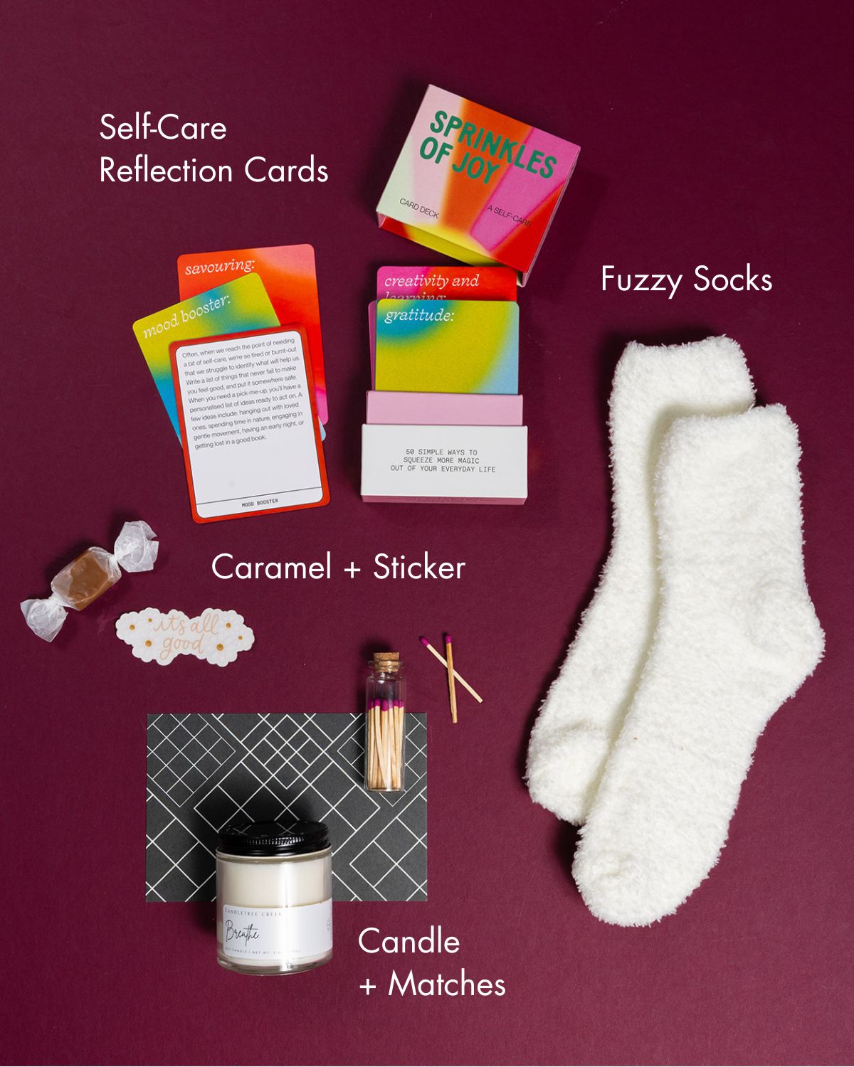 Me Time self-care gift set with fuzzy white socks, a scented candle, matches, caramel, a sticker, and colorful reflection cards.
