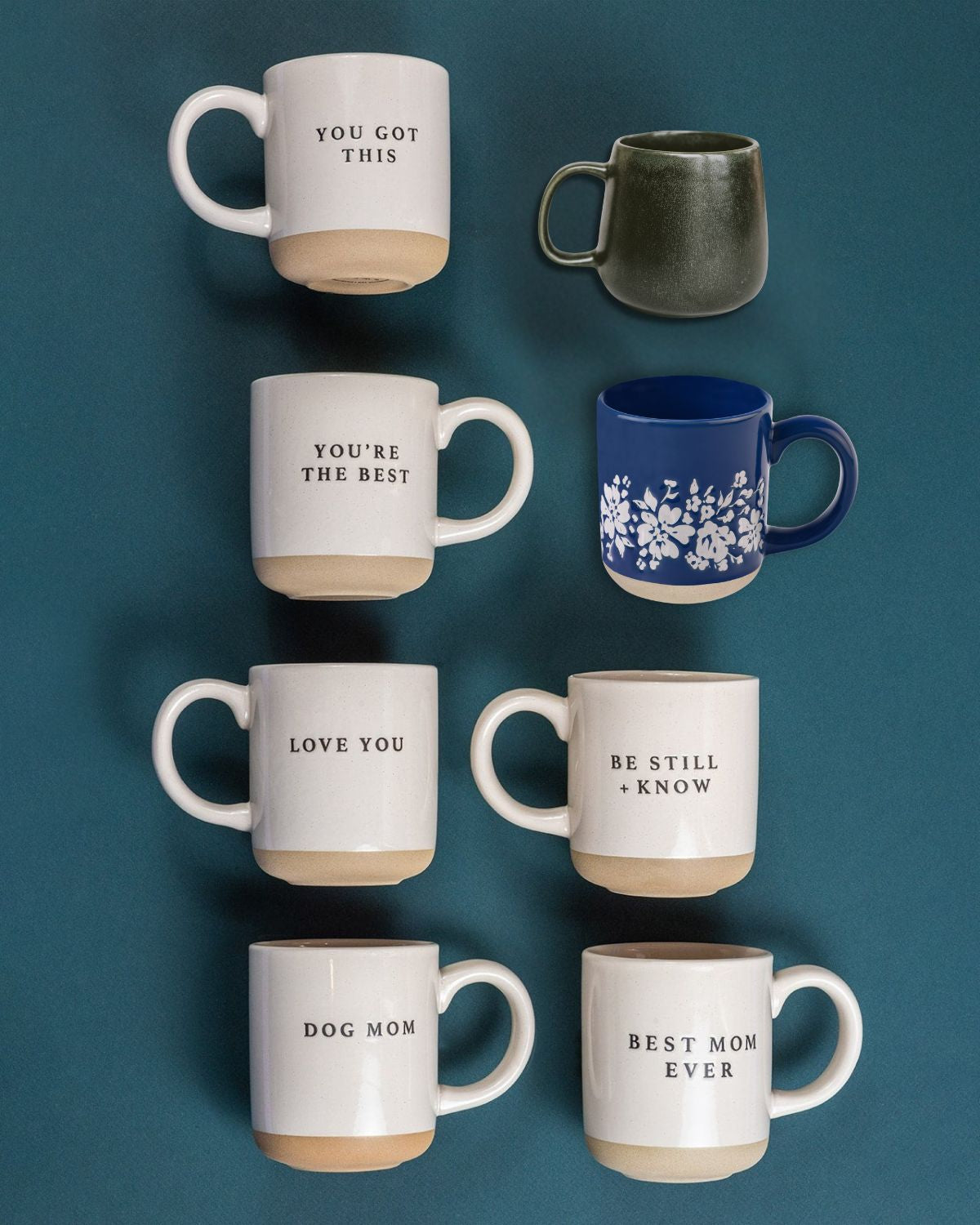 Collection of ceramic mugs in cream, dark green, and blue with floral patterns and inspirational text on a teal background.