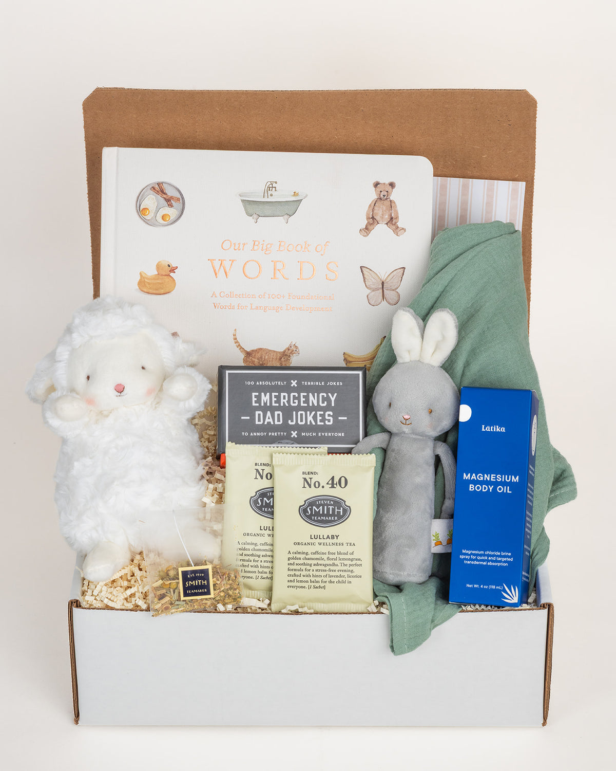 New baby gift box featuring a board book, plush lamb, bunny rattle, muslin swaddle, magnesium oil, and lullaby tea packets.