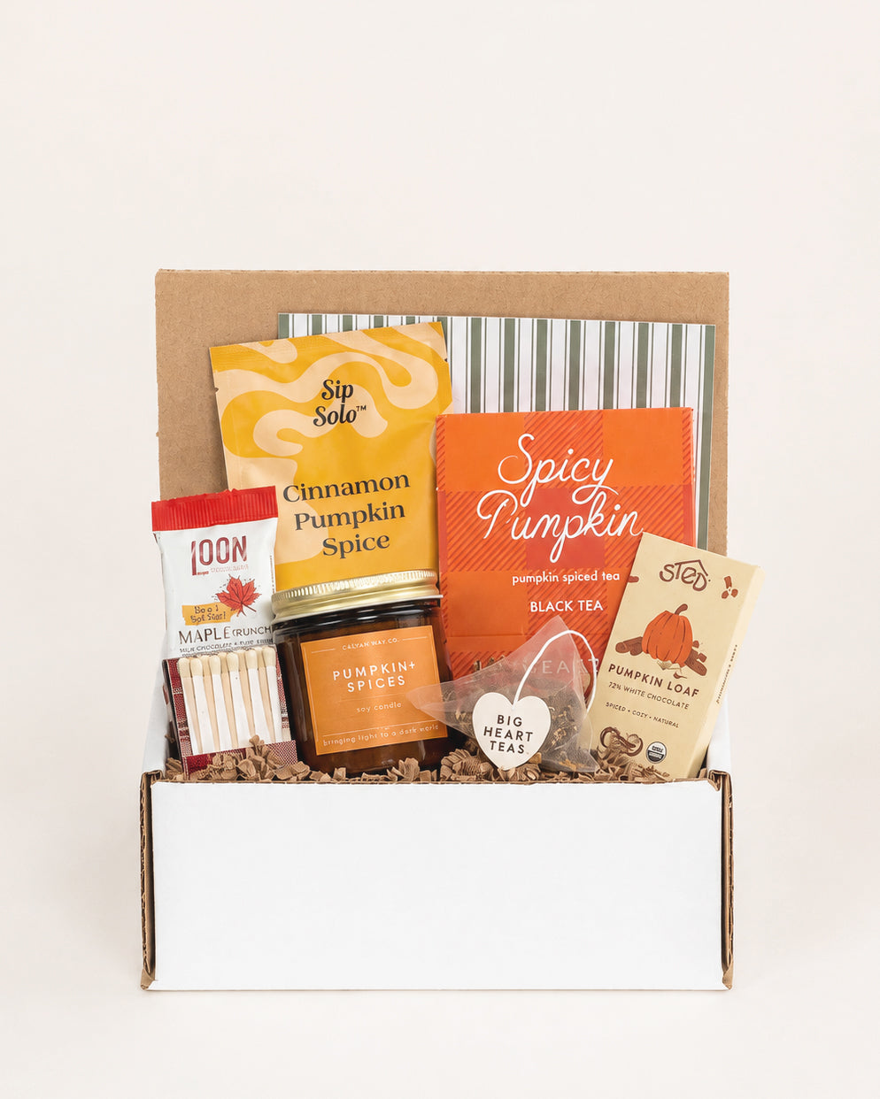 Pumpkin Season gift box featuring a soy candle, pumpkin spiced tea, chocolate bars, and matches nestled in brown crinkle paper.