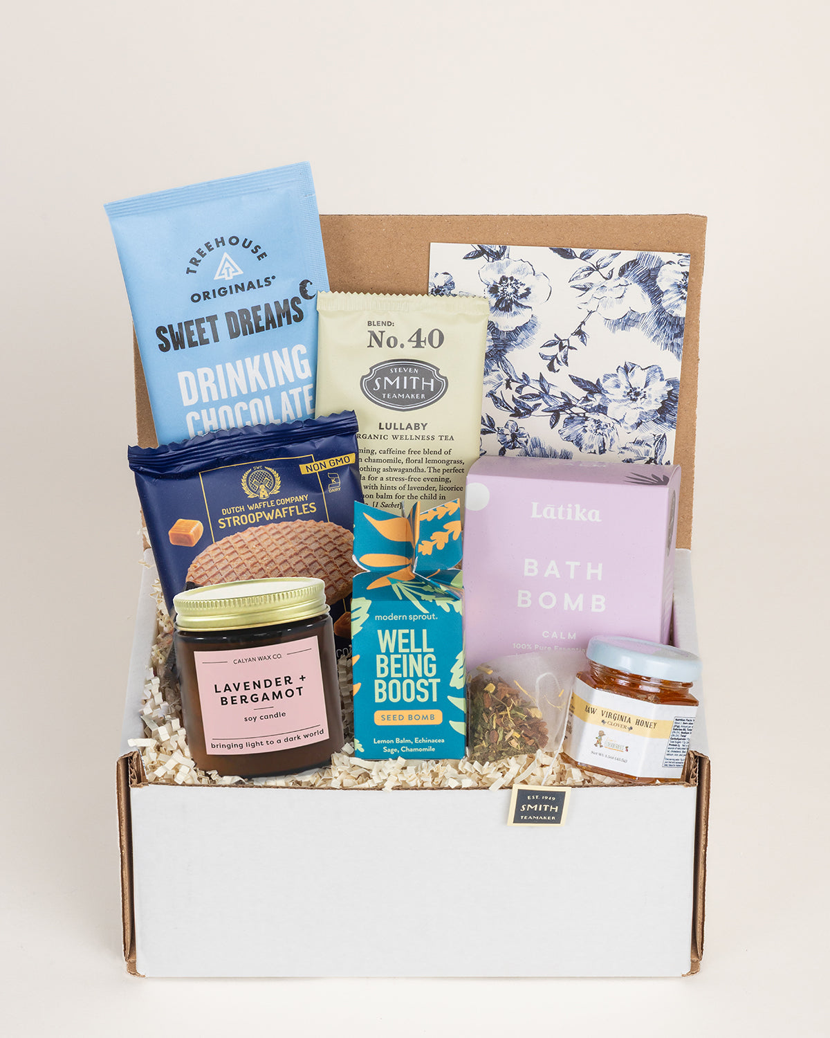 Self-care gift box containing a lavender candle, bath bomb, herbal tea, drinking chocolate, stroopwaffles, honey, and seed bomb.