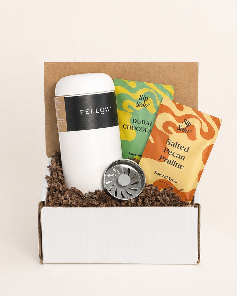 White Fellow travel tumbler with two Sip Solo flavored syrup packets in a gift box filled with brown paper crinkle.