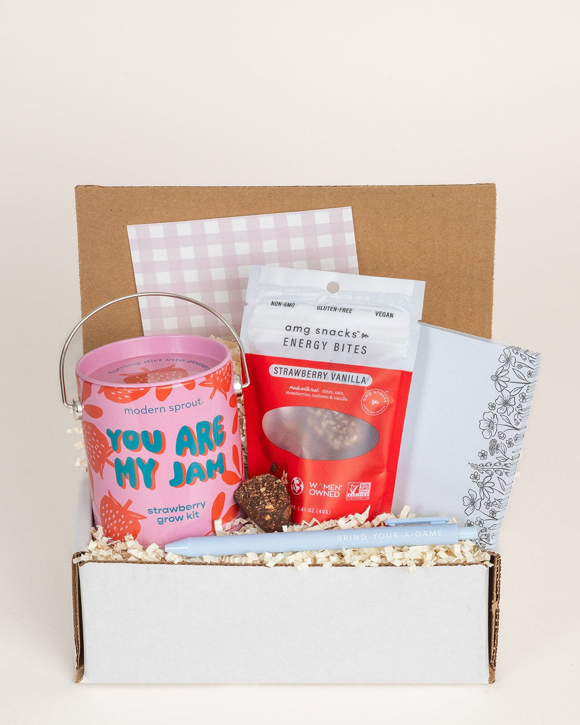 Strawberry grow kit, energy bites, floral notepad, and a light blue pen packed in a gift box with crinkle paper.