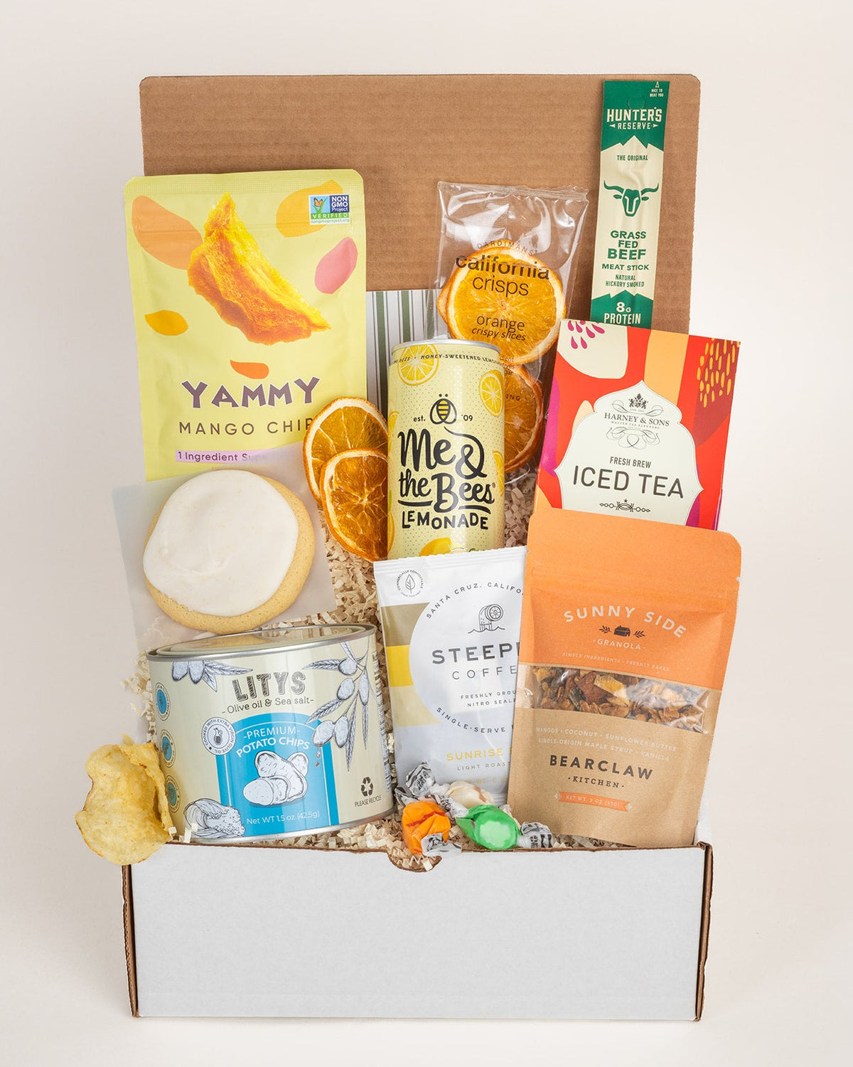 Summer gift box filled with assorted snacks, including mango chips, lemonade, iced tea, coffee, and cookies in a cardboard crate.