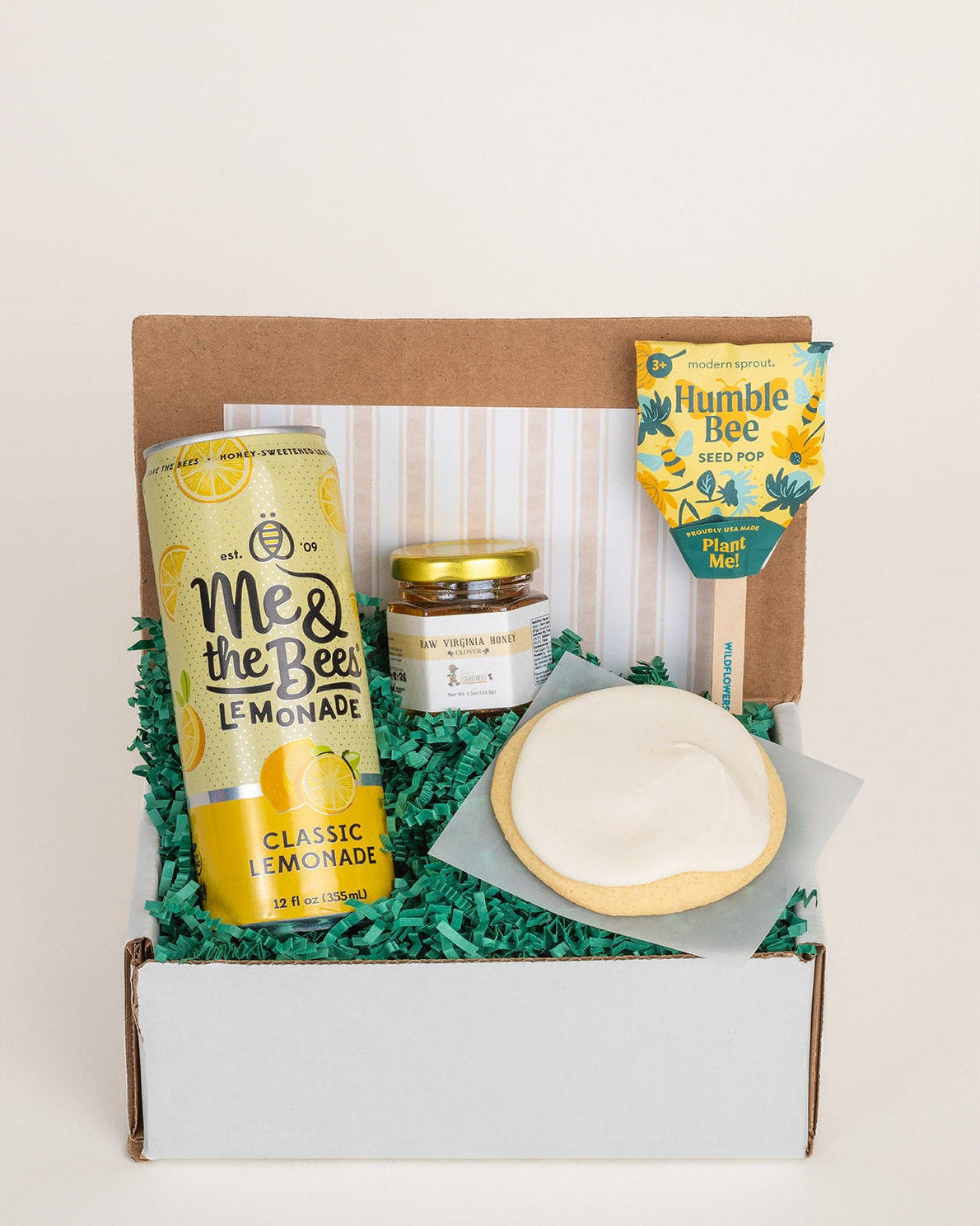 The Bee's Knees gift box with lemonade, honey, a lemon cookie, and a plantable seed pop nestled in green paper shred.