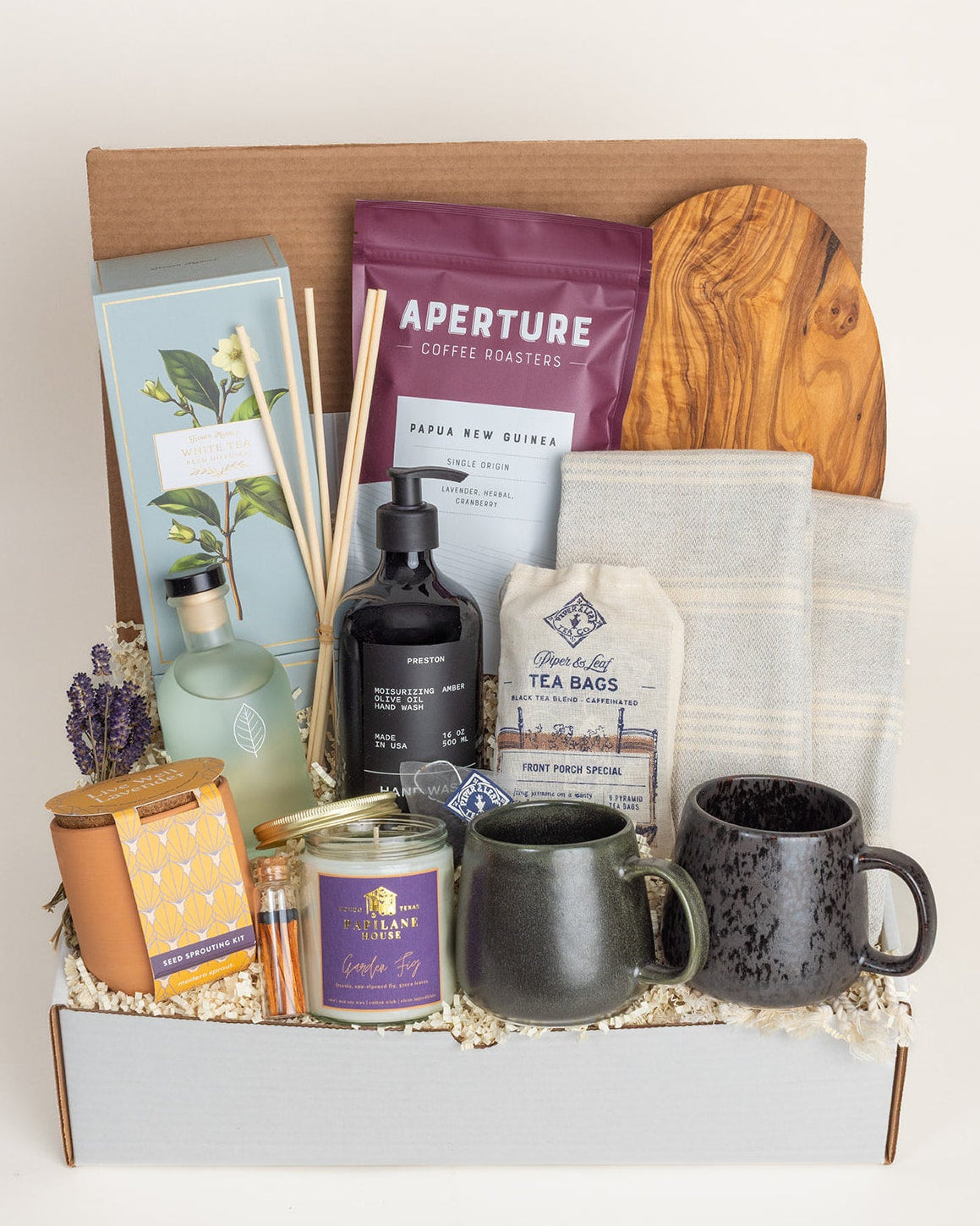 Curated gift box featuring olive wood board, ceramic mugs, Turkish towels, coffee, tea, candle, and lavender sprouting kit.