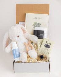 Welcome Baby gift box with a plush white bunny, wooden teether, board book, herbal tea, lavender bath salts, and baby lotion.