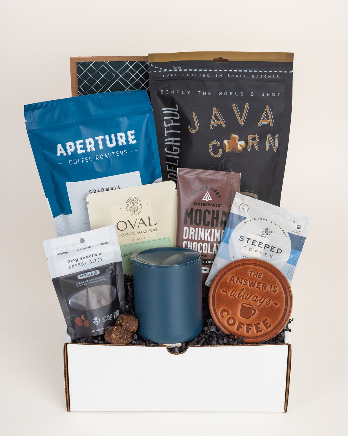 Coffee gift box featuring a blue tumbler, leather coaster, java popcorn, and assorted coffee snacks in a white box.