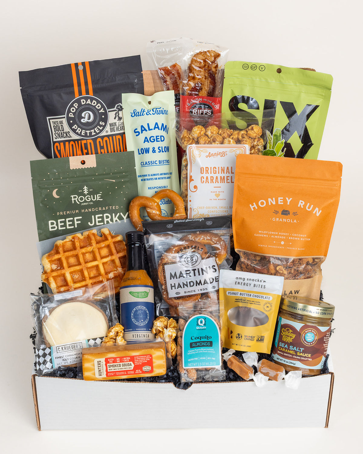 Deluxe Foodie gift box filled with assorted gourmet snacks, beef jerky, pretzels, caramel sauce, and savory treats in a white box.