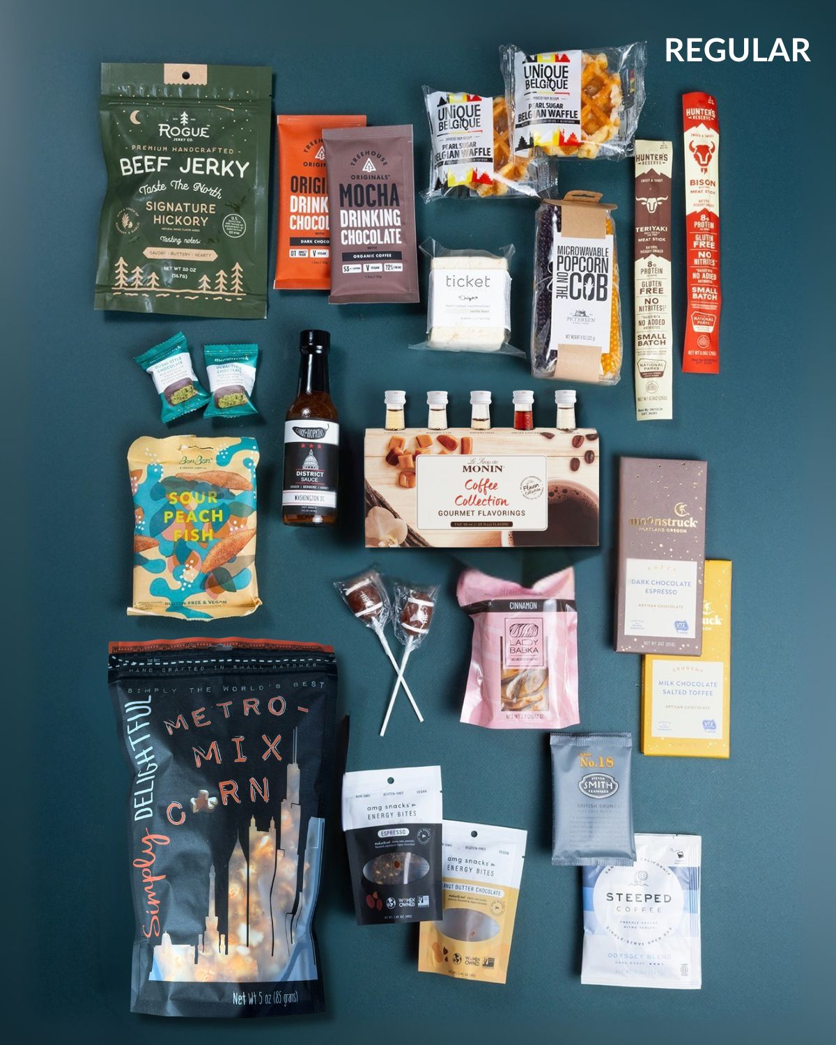 Large office gift box filled with assorted snacks, gourmet coffee syrups, beef jerky, chocolate bars, and popcorn on a dark teal background.