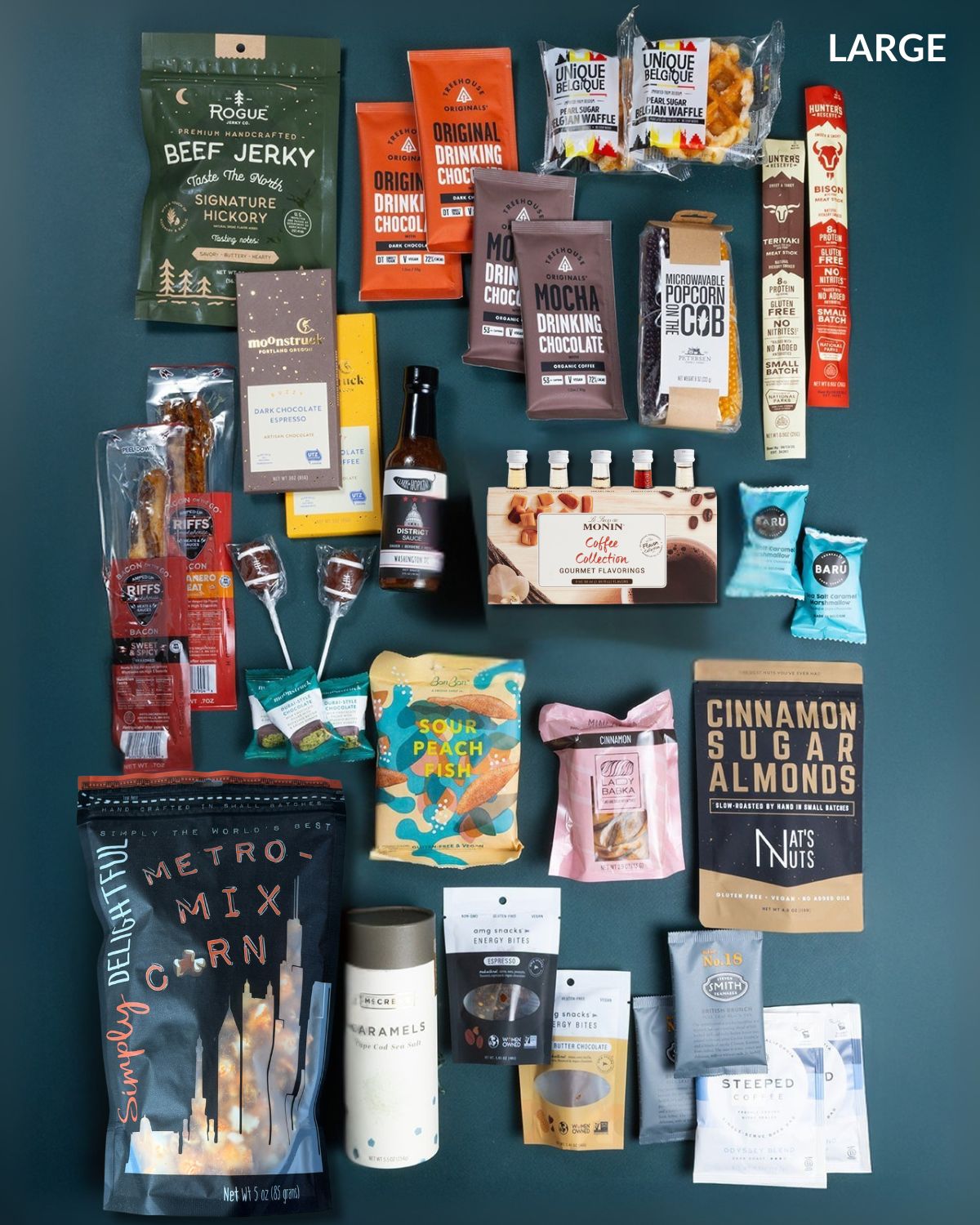 Large gift box filled with assorted gourmet snacks, coffee syrups, beef jerky, chocolates, and treats on a dark background.