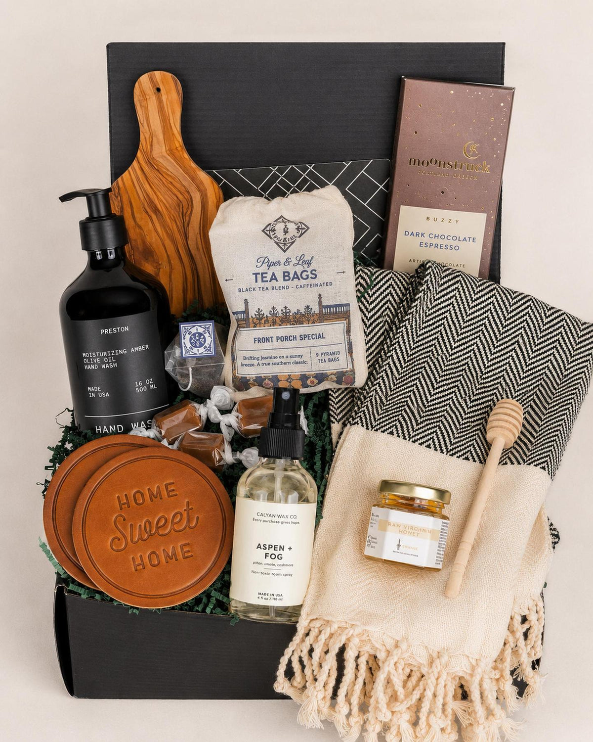 Hearth & Home gift box with olive wood board, tea, leather coasters, hand soap, chocolate, and a black and white patterned towel.