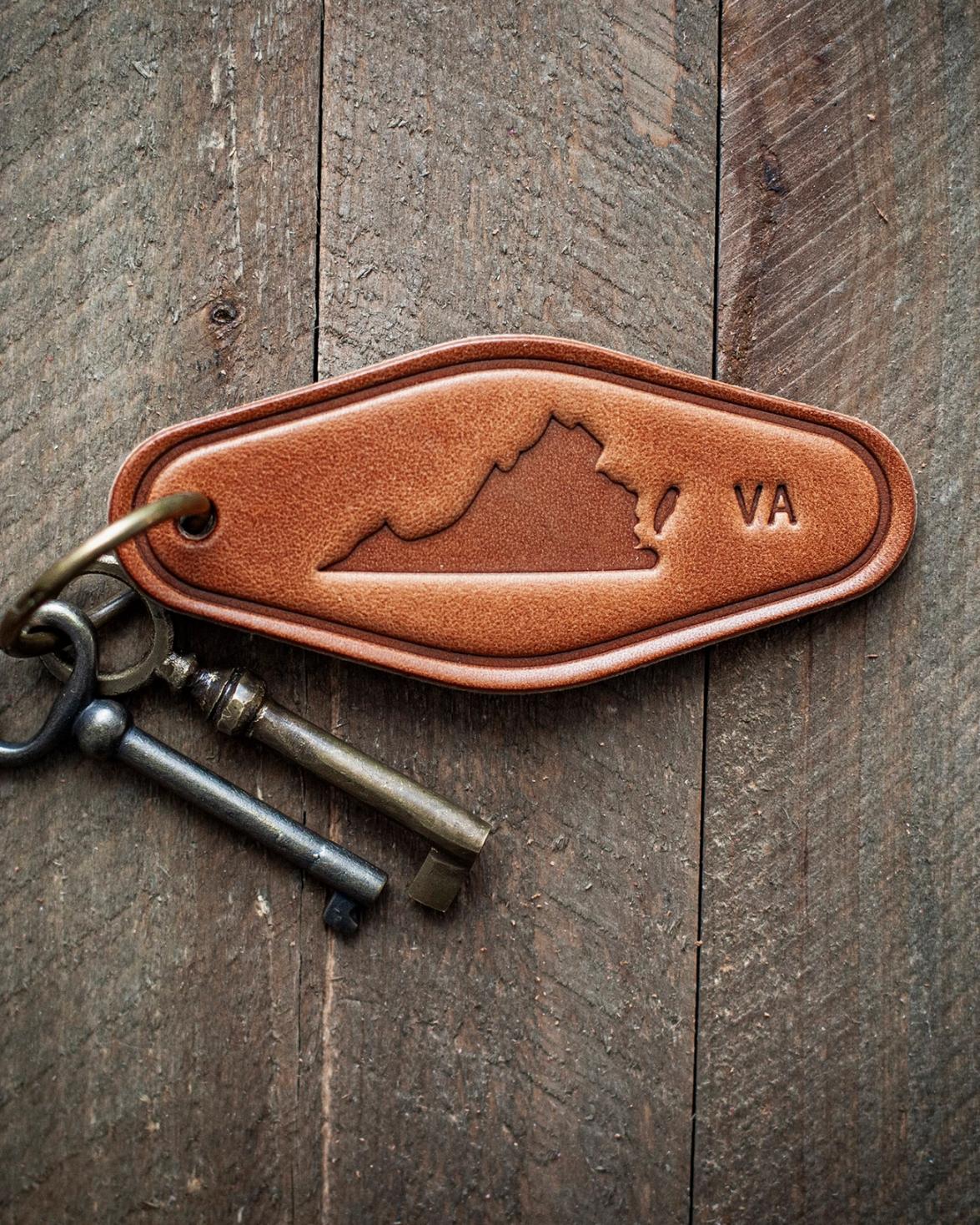 Tan leather keychain embossed with a Virginia state map and VA text, attached to vintage metal keys on rustic wood.