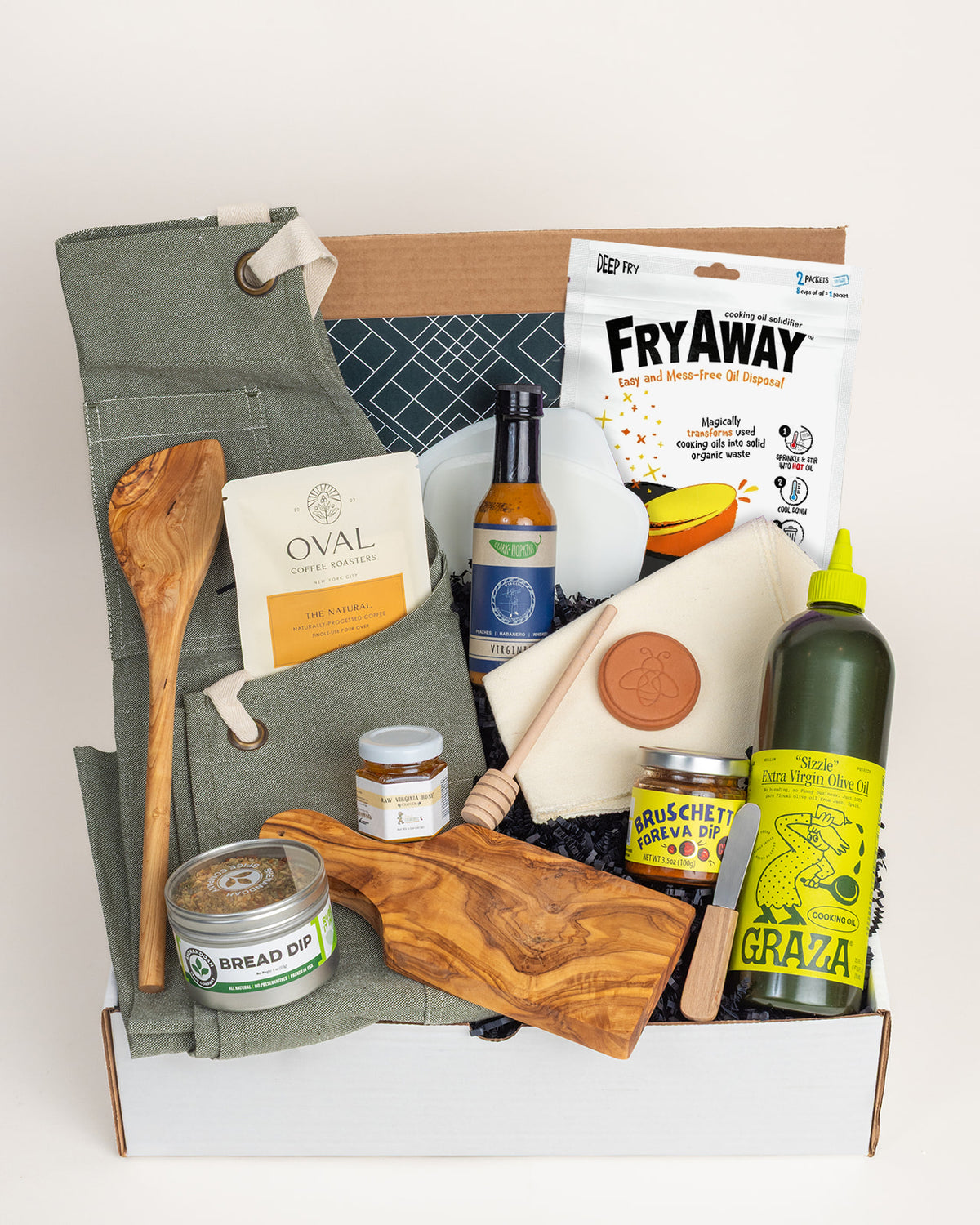 Curated kitchen gift box featuring a sage apron, olive wood board, Graza olive oil, honey, and cooking essentials.