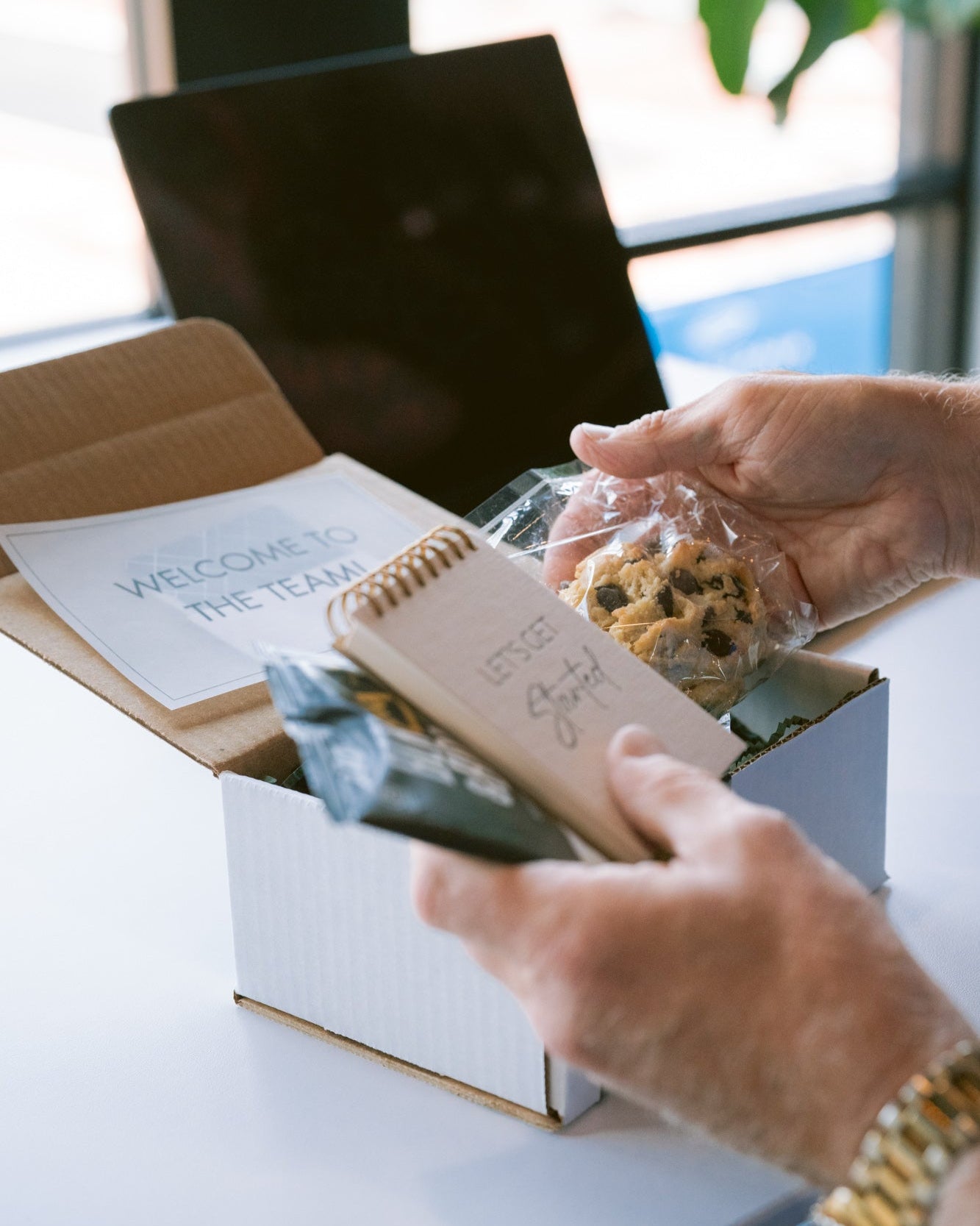 Person opening a box containing a spiral notebook and snacks, with a blurred background.