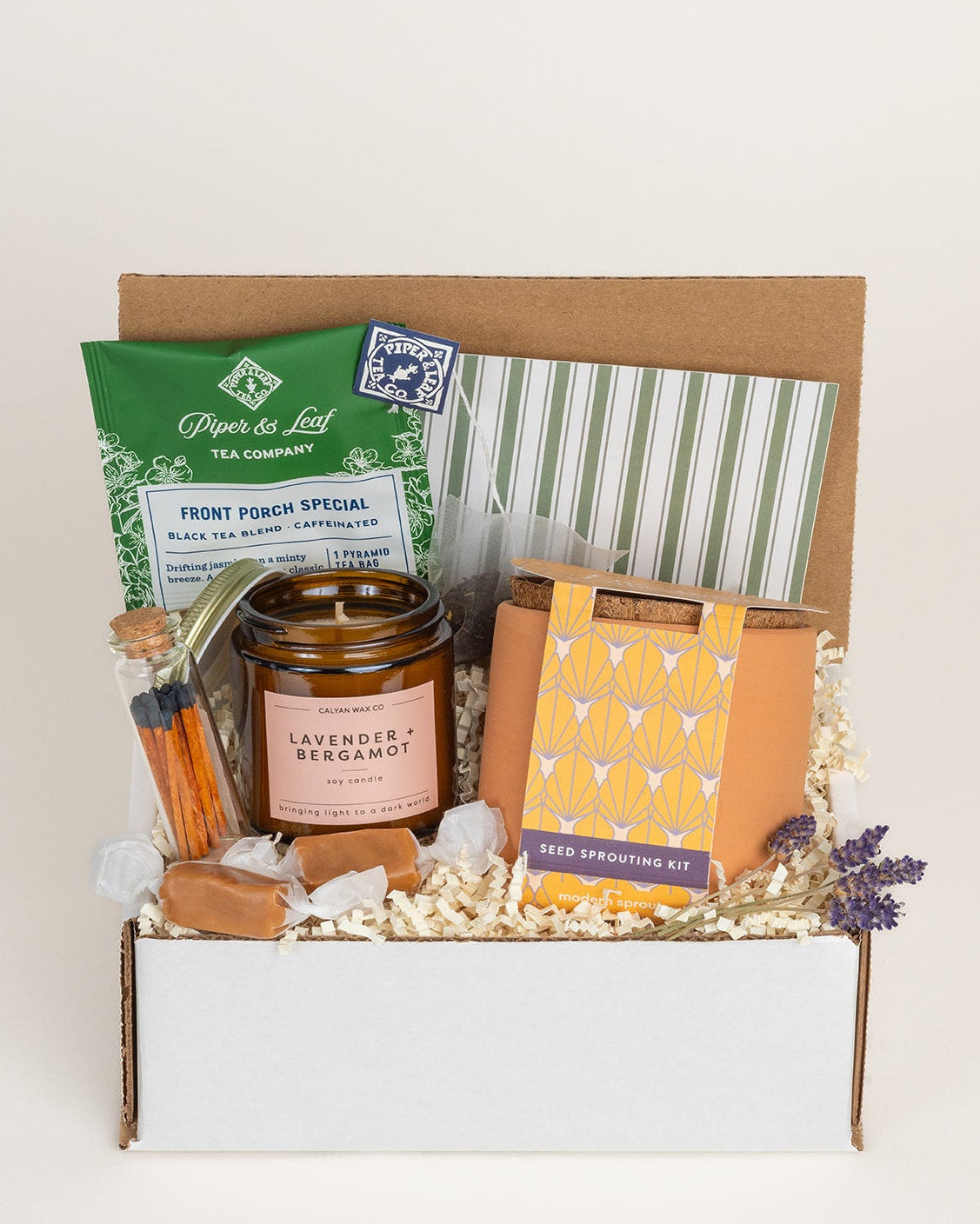 Gift box with lavender candle, seed sprouting kit, tea, caramels, and matches nestled in shredded paper filler.
