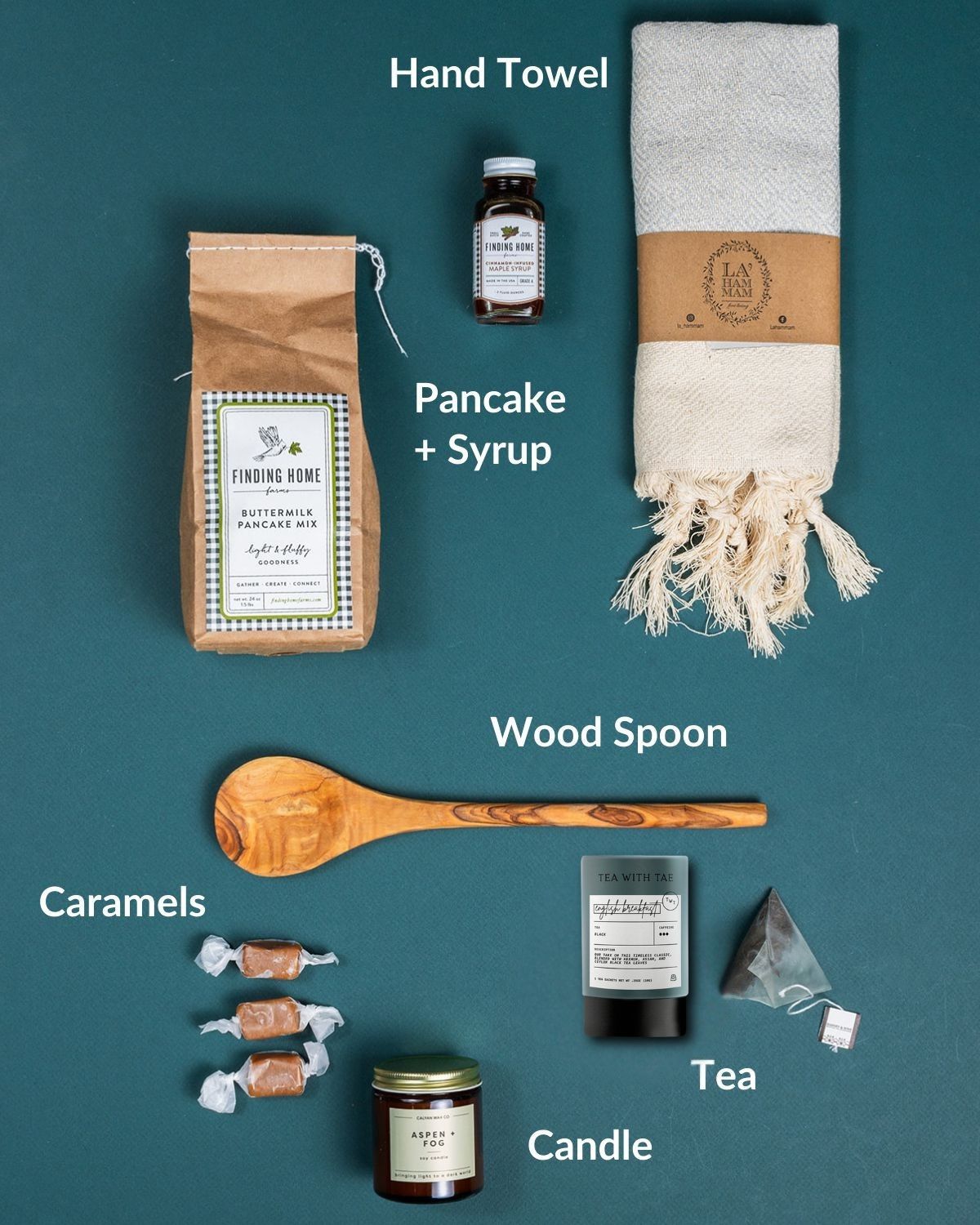 Pancake breakfast gift set with buttermilk mix, maple syrup, tasseled hand towel, olive wood spoon, tea, candle, and caramels.