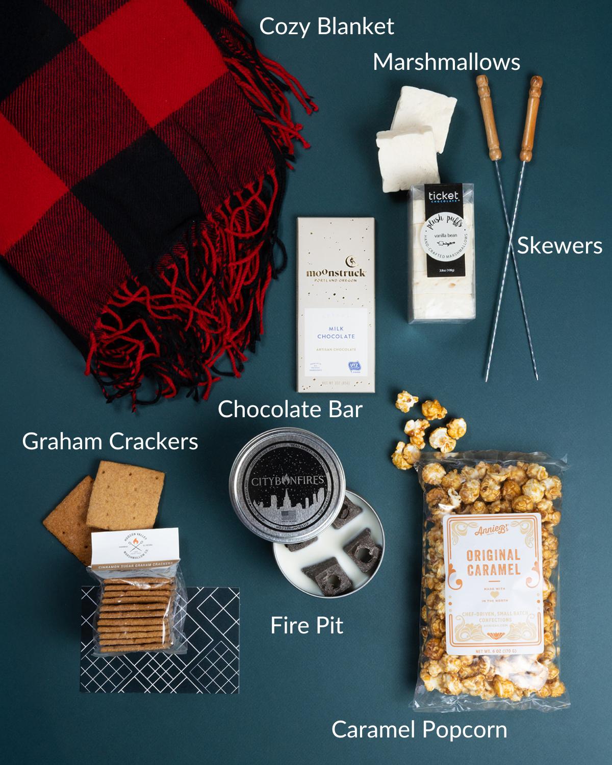 S'mores gift set with red plaid blanket, mini fire pit, chocolate bar, marshmallows, skewers, graham crackers, and caramel popcorn.